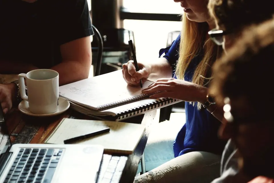 Two colleagues reviewing notes beside a laptop