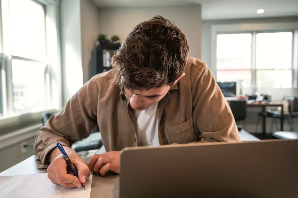 A man writing a plan by hand next to his laptop